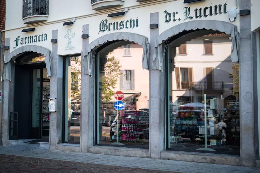 Vista esterna della farmacia Bruschi Dr. Lucini, con tre grandi vetrine che mostrano prodotti e un'insegna sopra.